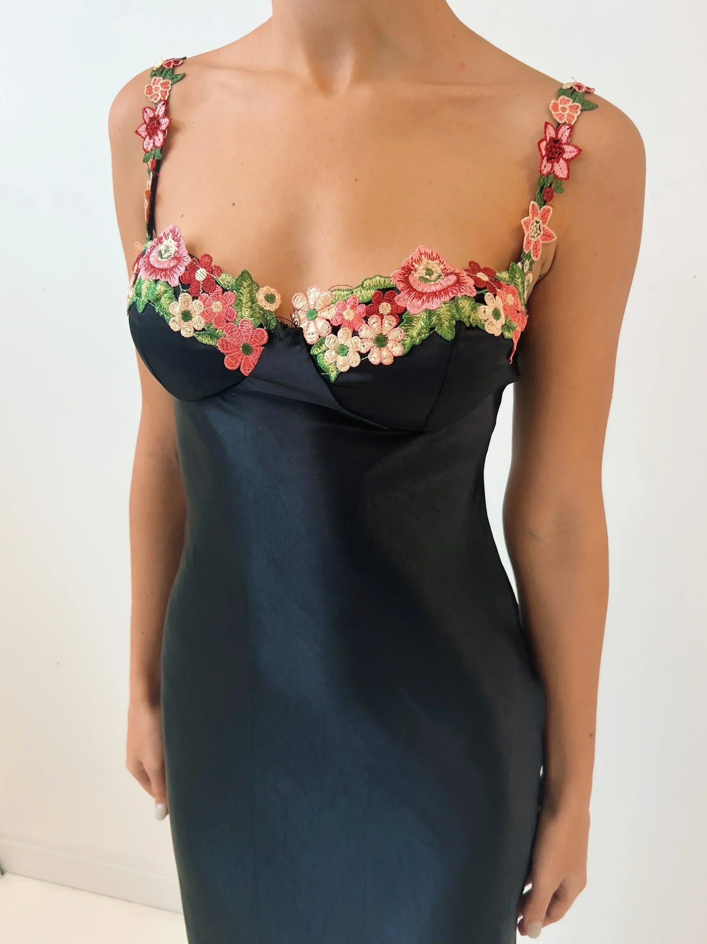 Robe longue en tissu léger, noire, ornée de broderies florales colorées sur les manches et le bas.