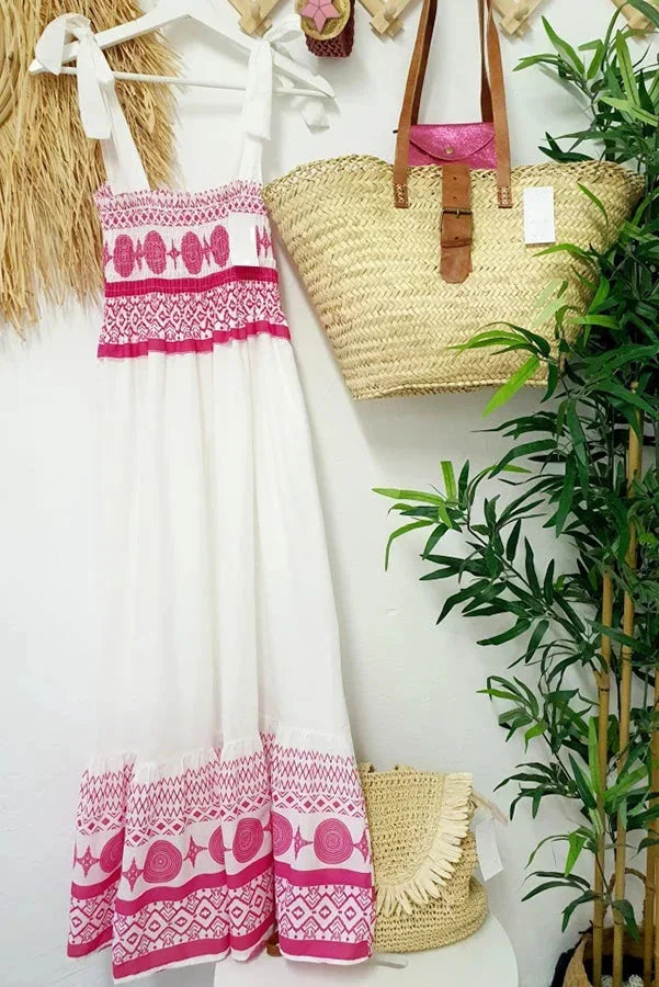 Robe longue blanche sans manches avec motifs tribaux roses, encolure carrée, idéale pour l'été et les journées à la plage.