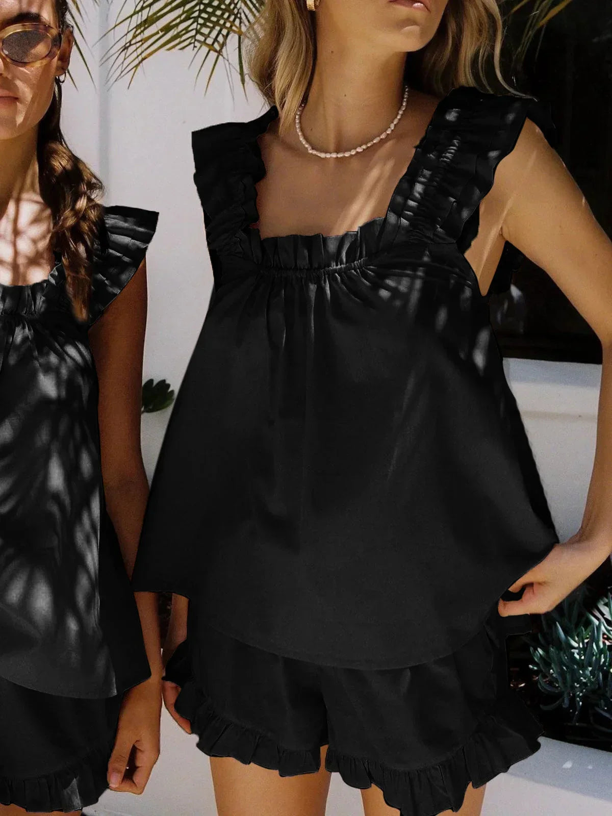 Ensemble femme noir en tissu léger, haut sans manches avec volants et short assorti, idéal pour les journées chaudes.