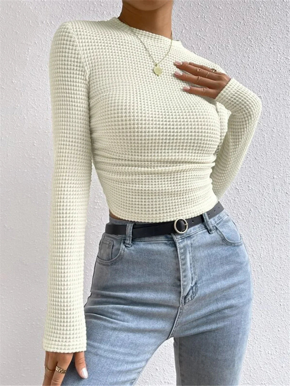 Haut beige à manches longues en maille texturée, au design moderne et minimaliste, adapté pour les journées fraîches.