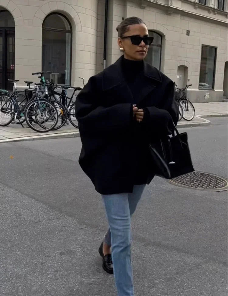 Manteau ample noir en mélange de laine, avec grands revers et boutons décoratifs.
