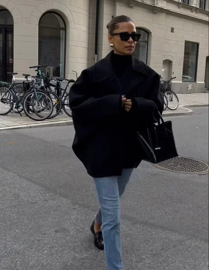 Manteau ample noir en mélange de laine, avec grands revers et boutons décoratifs.
