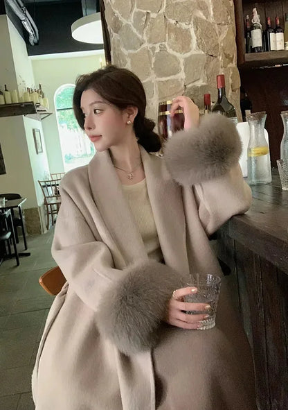 Manteau long noir pour femme, ceinturé, avec manches en fausse fourrure.