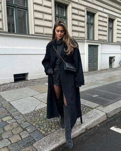 Manteau long noir femme en laine avec ceinture et larges revers pour une silhouette ajustée.