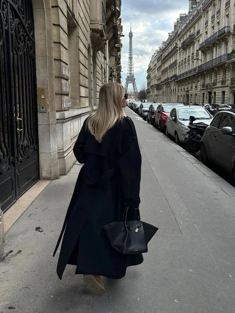 Manteau long noir femme avec ceinture, larges revers et tissu chaud, adapté pour les journées fraîches.