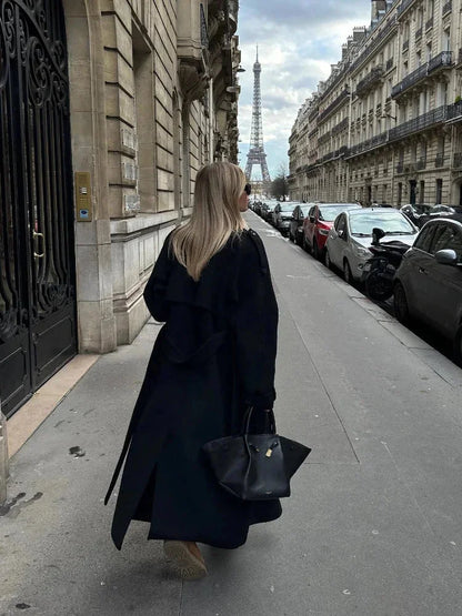 Manteau long noir femme avec ceinture, larges revers et tissu chaud, adapté pour les journées fraîches.