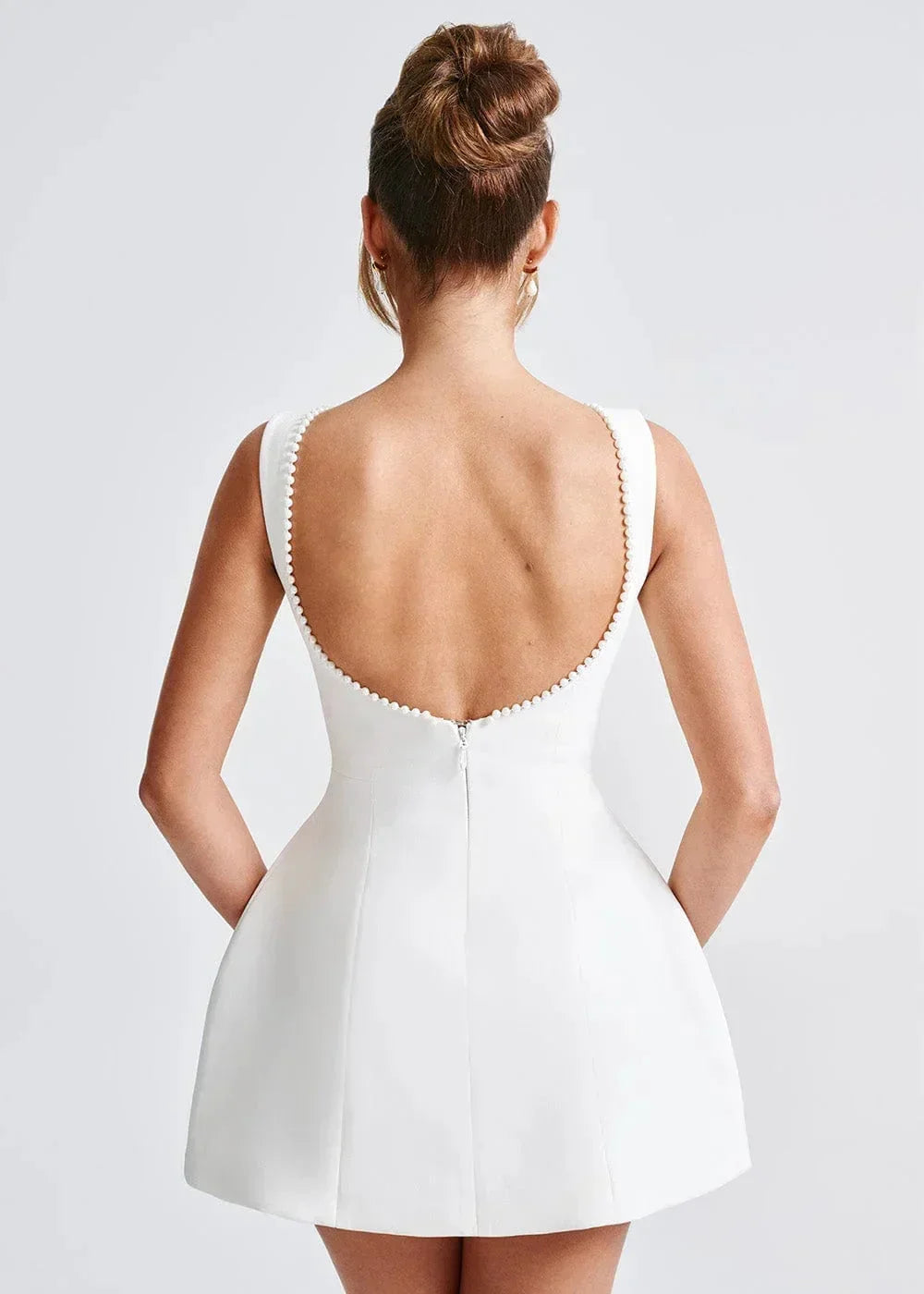Mini robe dos nu avec grand nœud, réalisée en tissu doux, coupe ajustée ornée de perles élégantes pour soirées.
