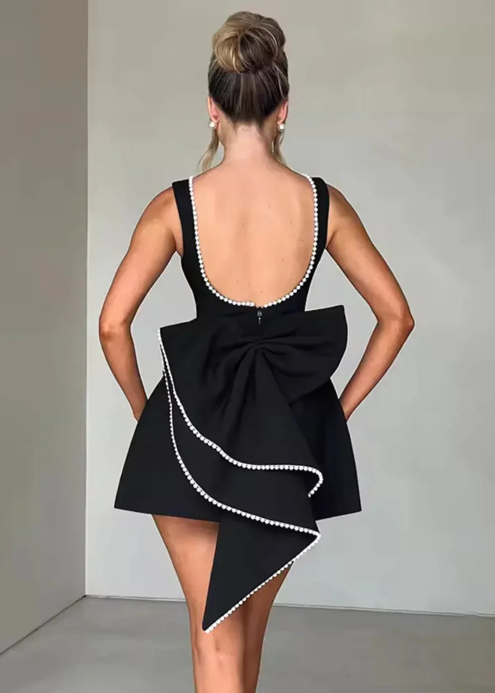 Mini robe dos nu ajustée avec un grand nœud, dotée de perles, idéale pour des soirées élégantes et décontractées.