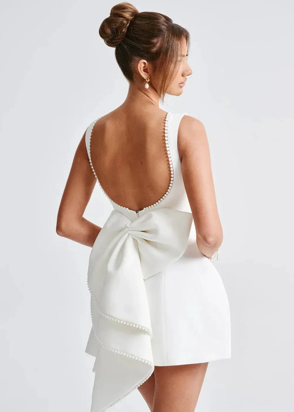 Mini robe dos nu ajustée avec grand nœud et perles, en tissu doux, idéale pour les soirées élégantes.