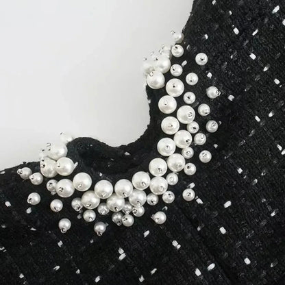 Mini robe noire perlée avec découpes, manches épaules nues, en tissu léger, idéal pour les soirées et événements.