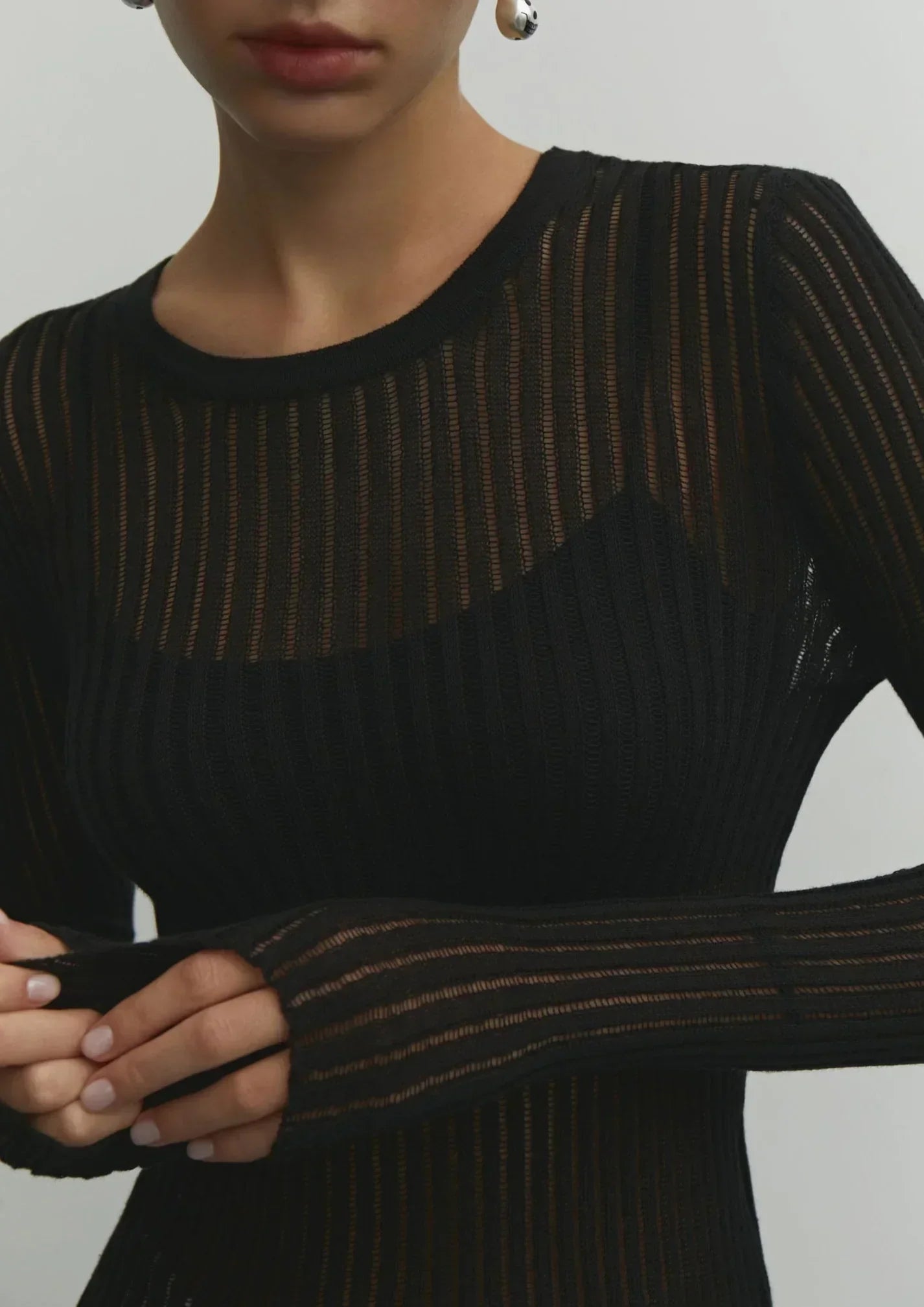Pull femme noir en maille côtelée, style décontracté avec des emmanchures longues et des motifs ajourés.