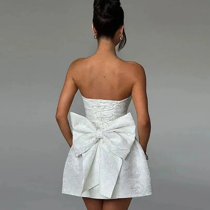 Robe courte femme bustier blanche avec dos lacé et nœud, en tissu léger, idéale pour les occasions estivales.