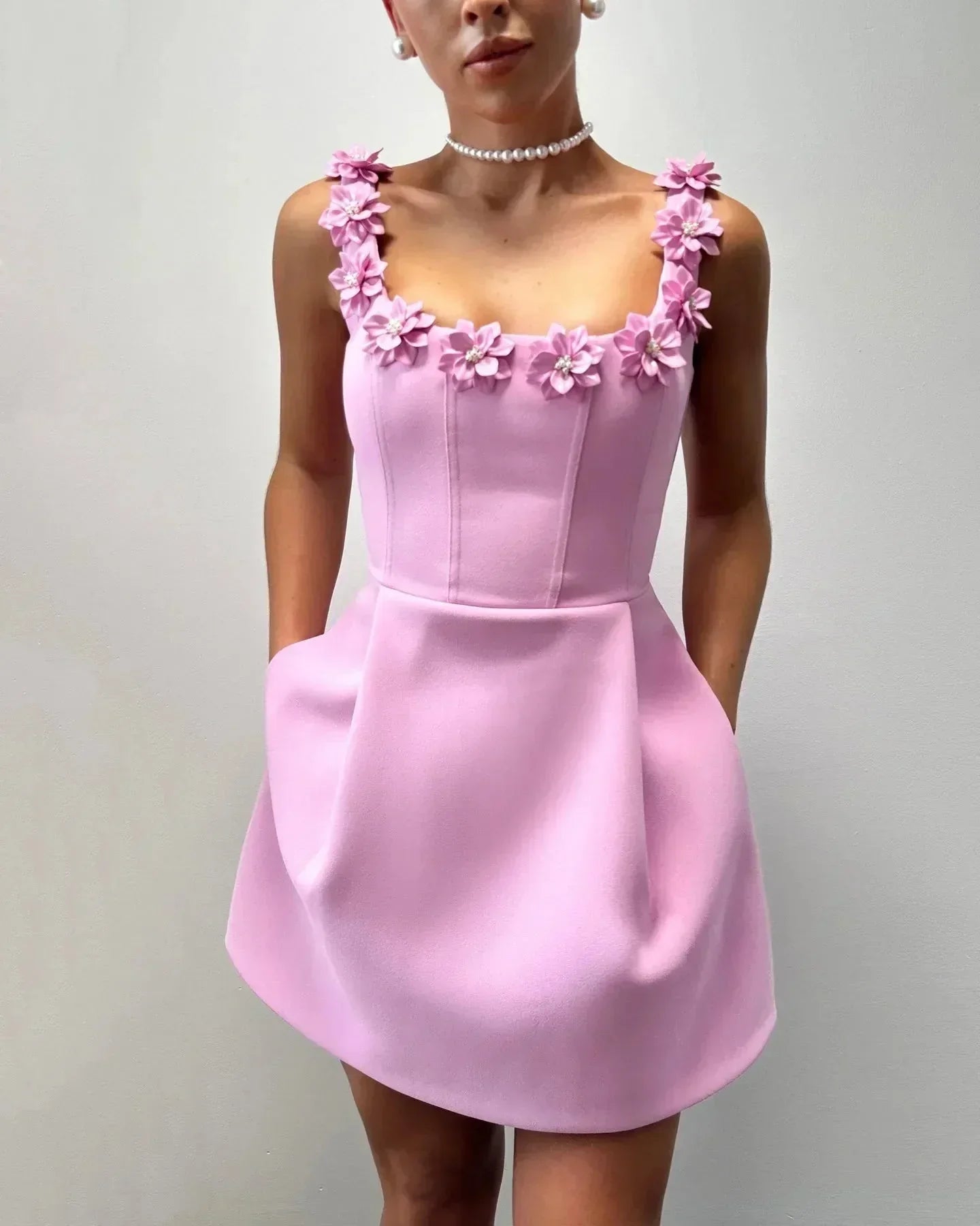 Robe courte sans manches rose avec détails floraux, en tissu léger, parfaite pour les fêtes d'été avec encolure ajustée.