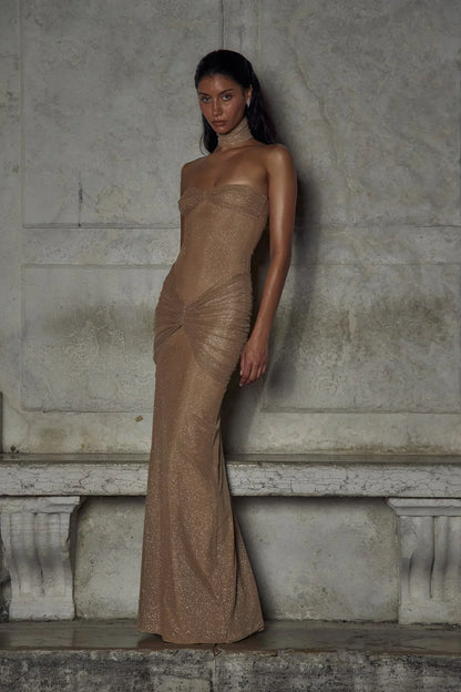 Robe longue beige sans bretelles en tissu scintillant avec plis élégants pour une soirée.