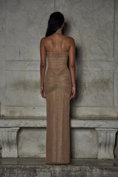 Robe longue beige sans bretelles en tissu scintillant, avec des plis élégants pour une silhouette raffinée.
