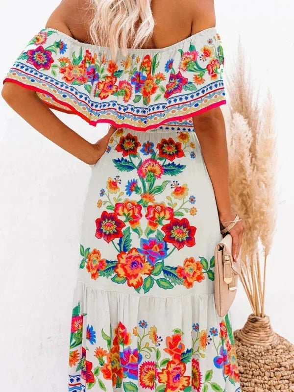 Robe longue femme en tissu léger à épaules dénudées, décorée de motifs floraux colorés sur un fond doux.