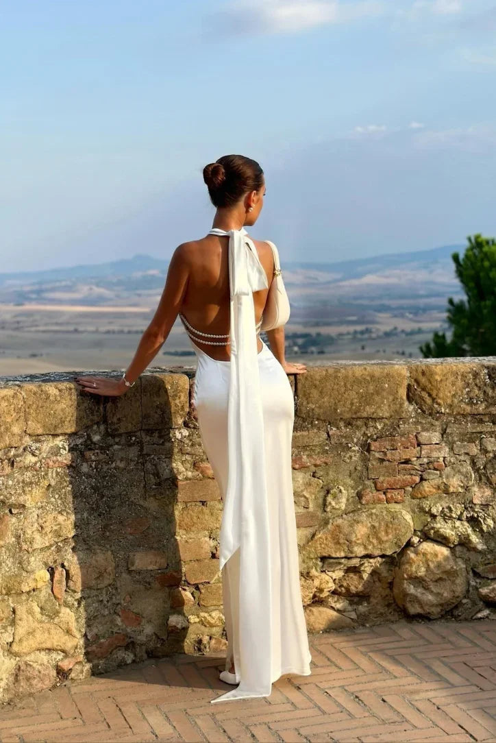 Robe longue blanche en tissu léger, dos ouvert, ornée de perles, parfaite pour une soirée d'été.