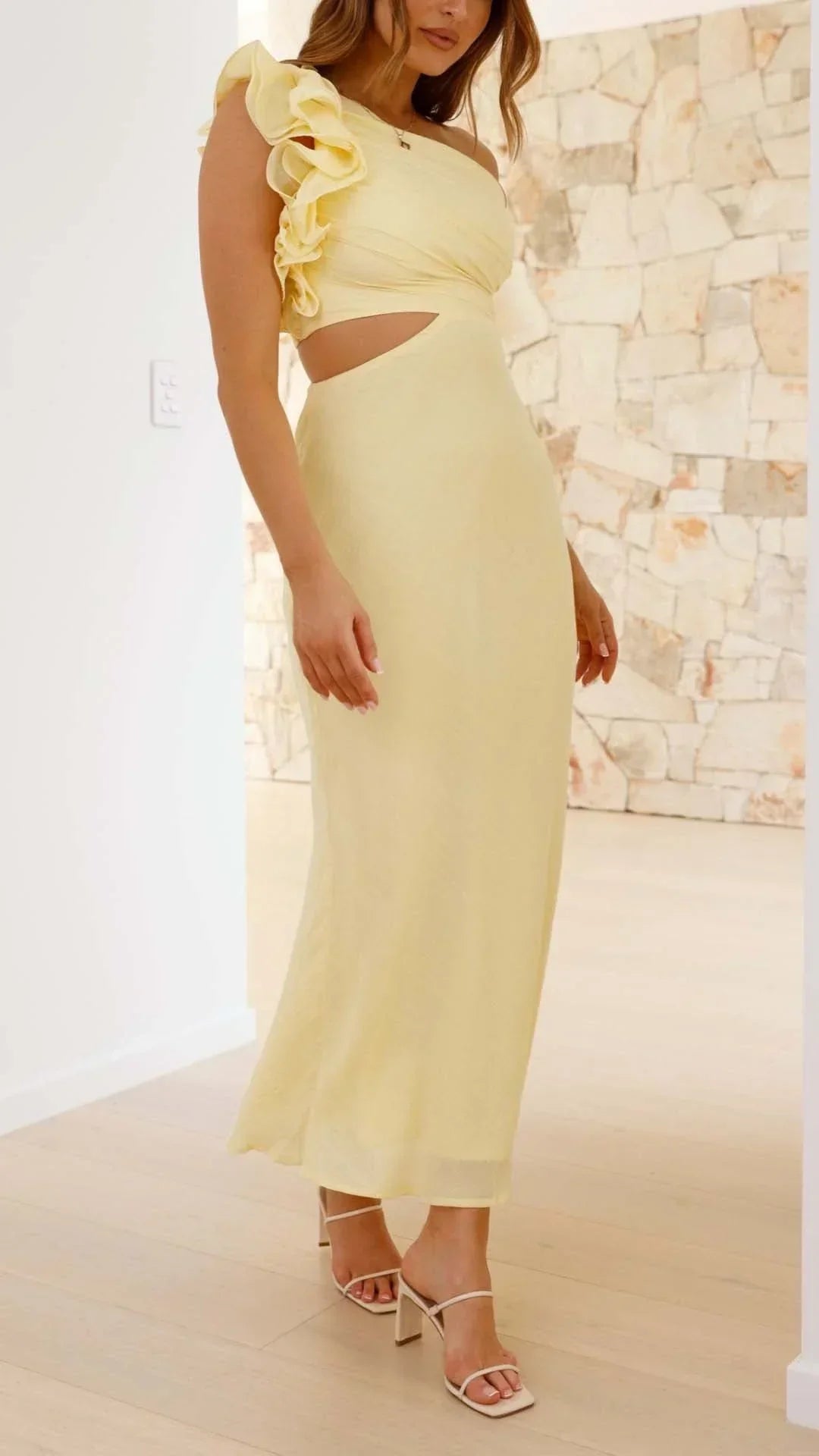 Robe longue jaune à une épaule, en tissu fluide, avec découpes élégantes et jambes dénudées pour une soirée chic.