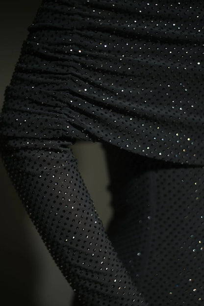 Robe longue longue scintillante avec épaules dénudées, manches longues et détails brillants en tissu léger et fluide.