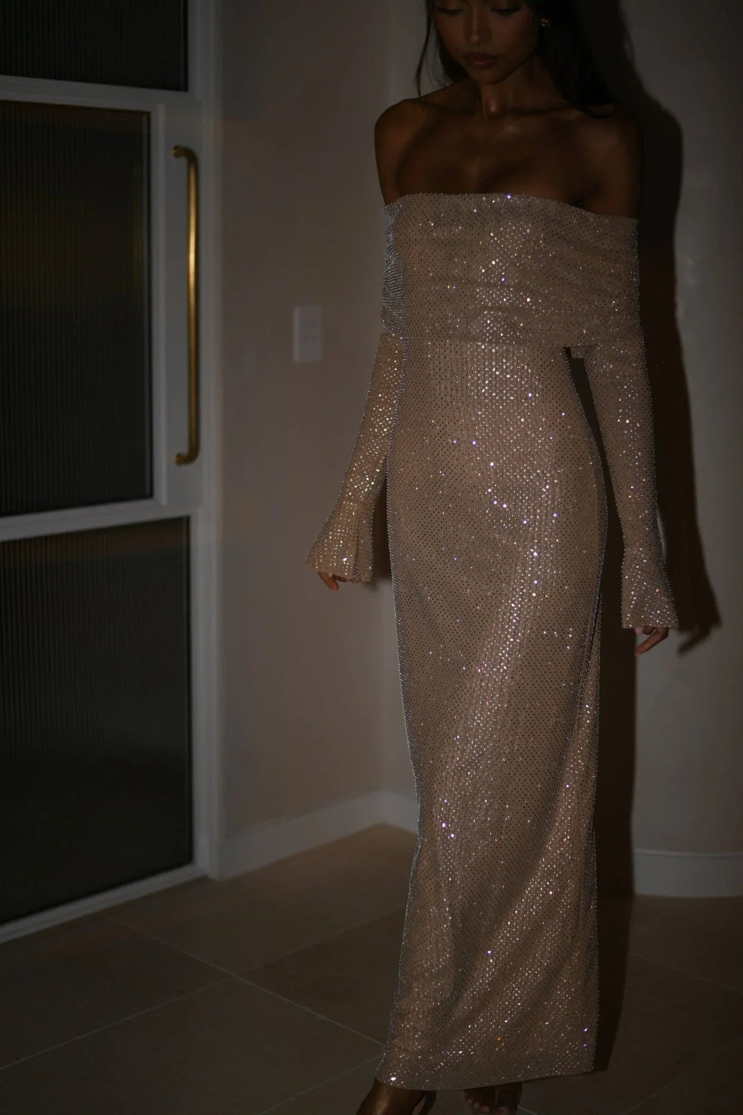Robe longue longue en tissu scintillant, épaules dénudées et manches longues avec détails brillants pour un look élégant.