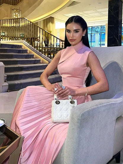 Robe longue plissée rose, sans manches, longueur sol, col asymétrique en tissu léger, idéale pour une tenue estivale.