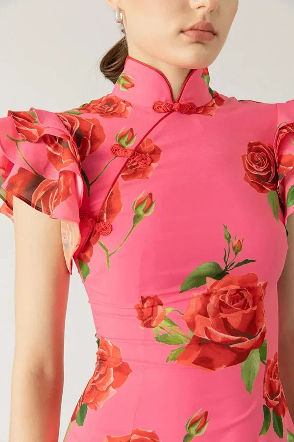 Robe longue rose avec motifs floraux, manches volantées, et col haut, confectionnée dans un tissu léger et fluide.