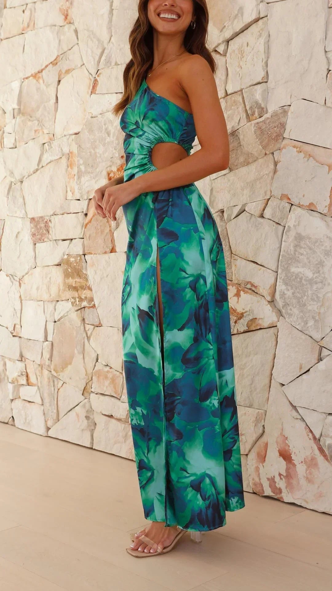 Robe longue verte à une épaule, fente latérale, en tissu léger, ornée d'un imprimé floral coloré.