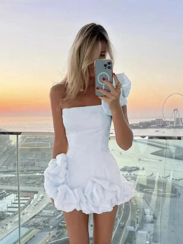 Robe courte asymétrique en tissu fluide, épaules dénudées et volants, idéale pour une soirée élégante.
