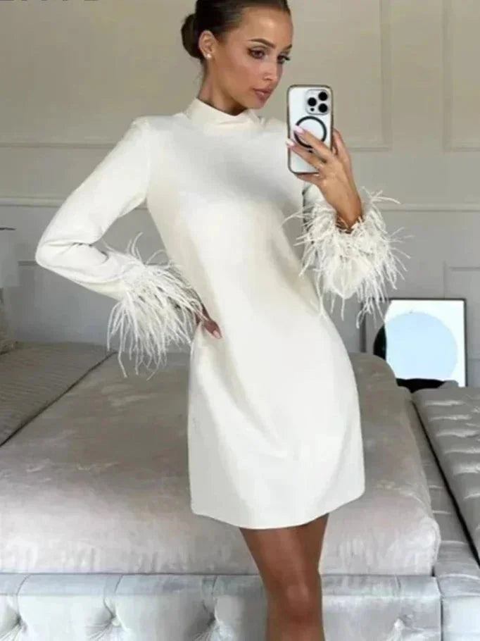 Robe courte blanche à manches longues en tissu léger, ornée de plumes, coupe droite élégante pour des événements.