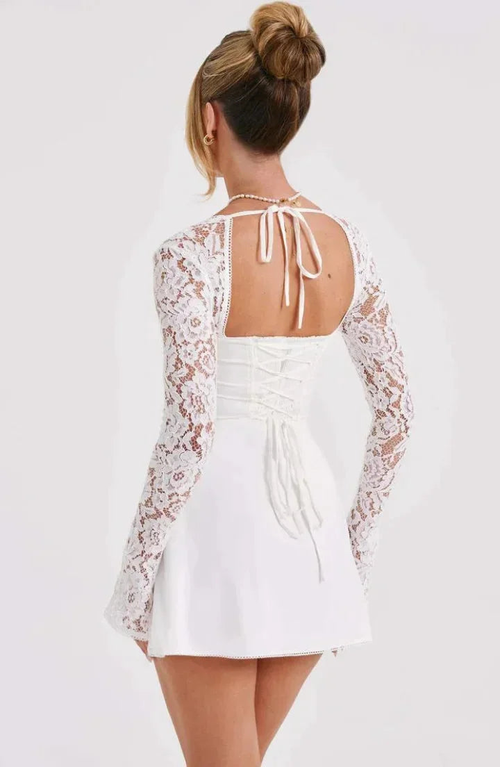 Robe courte blanche en dentelle, manches longues, dos nu, coupe ajustée pour un look élégant en soirée cocktail.
