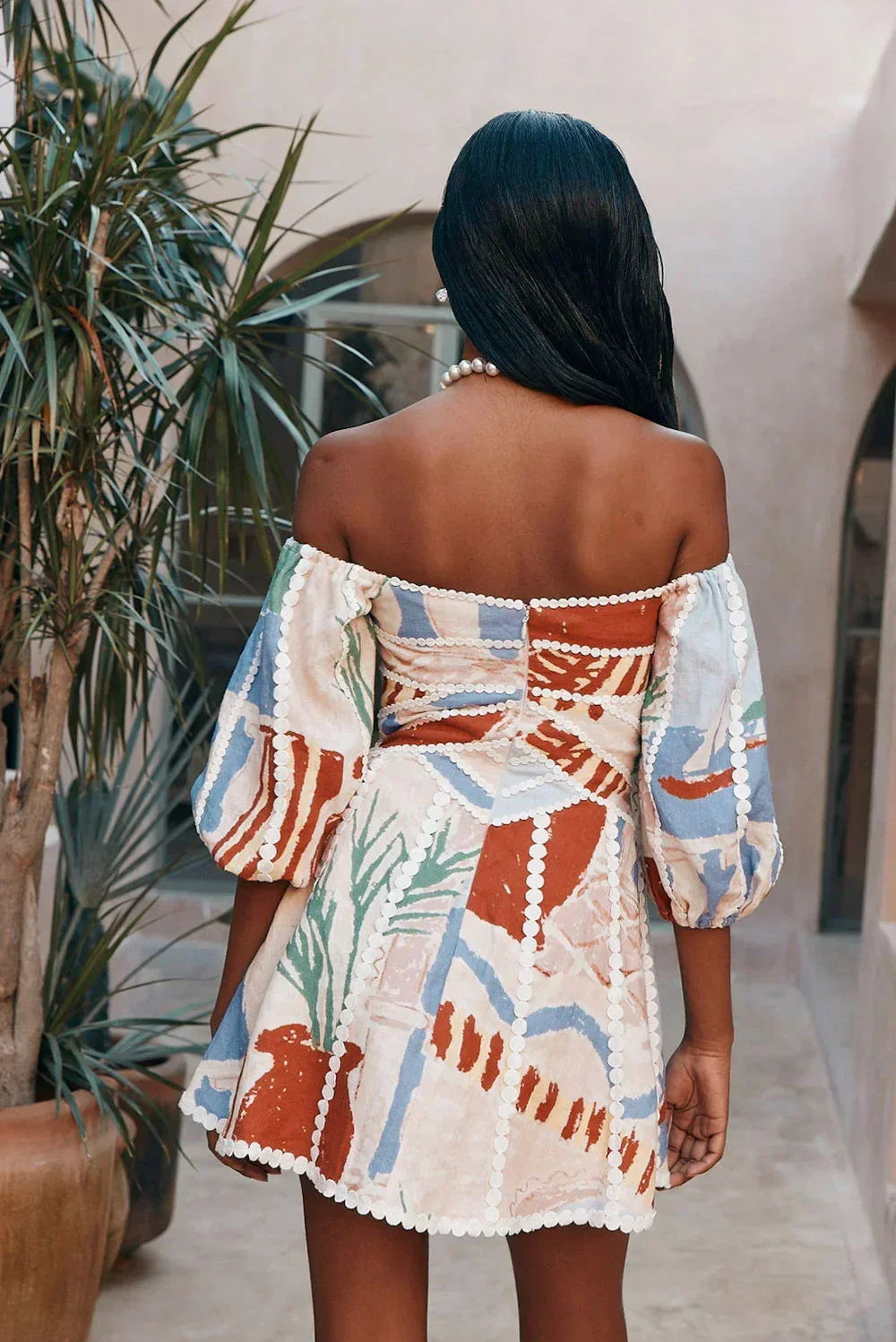 Robe courte blanche à manches bouffantes et épaules dénudées, tissu léger parfait pour les journées d'été à la plage.