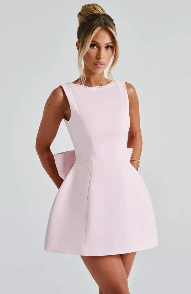 Robe courte dos nu ornée de perles et d'un gros nœud, confectionnée en tissu léger, disponible en plusieurs couleurs.