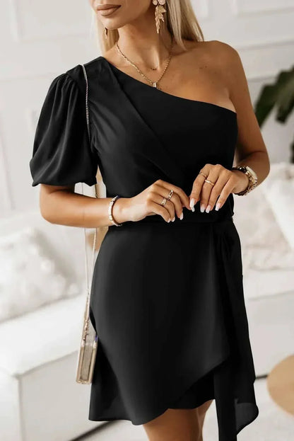 Robe courte noire, en tissu léger, avec encolure asymétrique et manches bouffantes, idéale pour une soirée élégante.