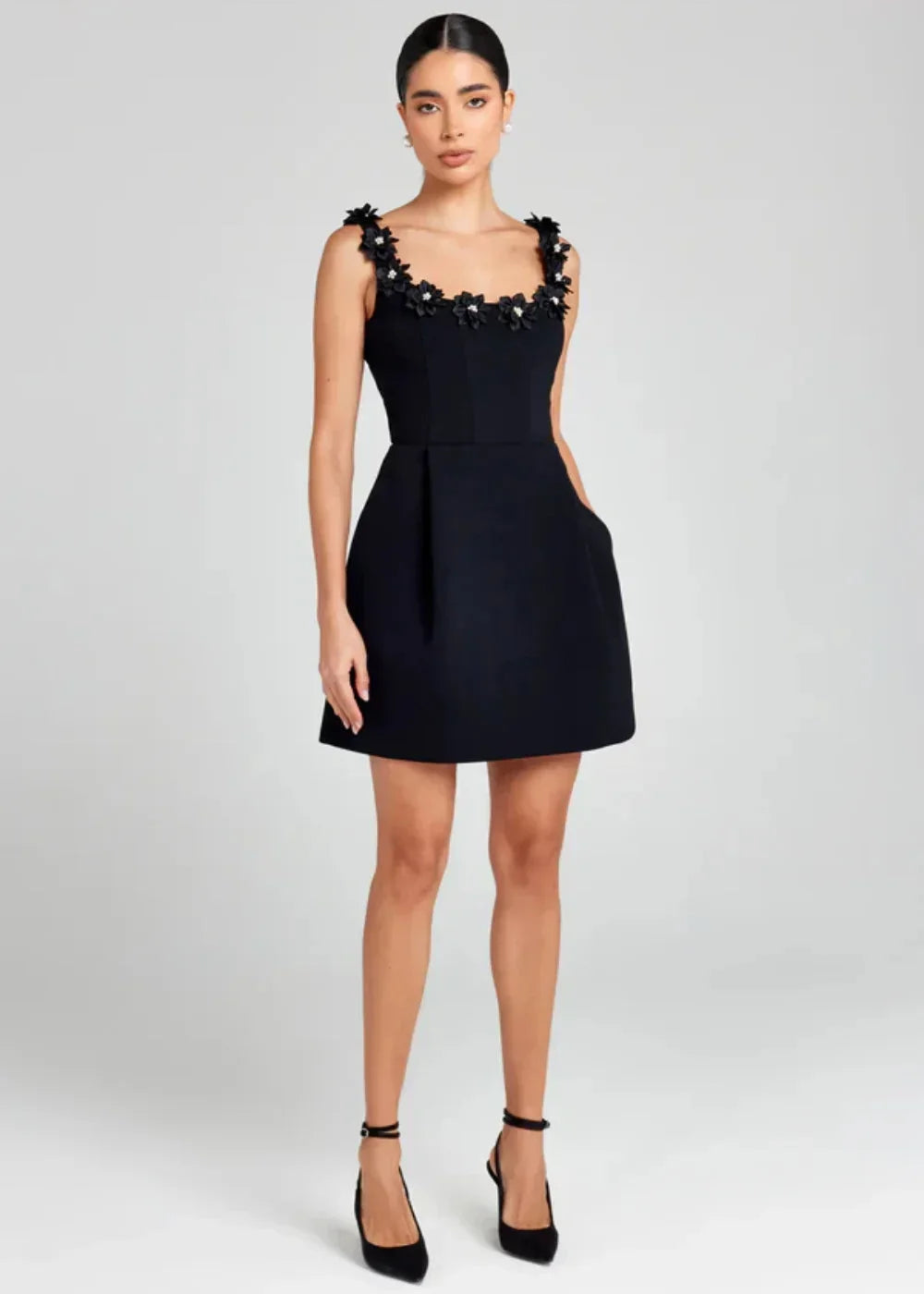 Robe courte noire sans manches, ornée de broderies de fleurs blanches, en tissu léger, idéale pour des événements élégants.