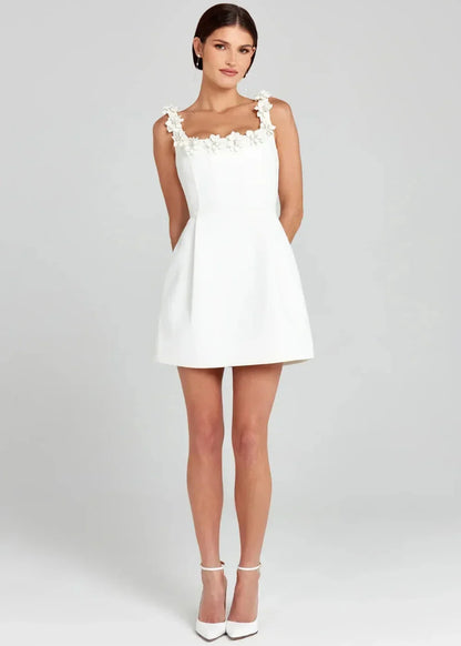 Robe courte noire sans manches avec broderies de fleurs blanches, en tissu léger, idéale pour les soirées élégantes.