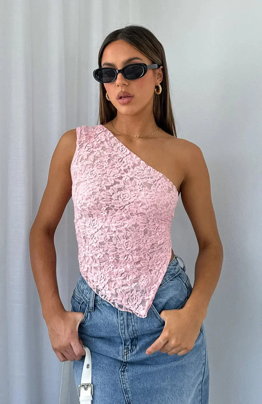 Top asymétrique en dentelle rose avec texture délicate et manches courtes, parfait pour une tenue élégante et féminine.
