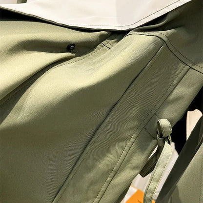 Veste coupe-vent verte pour femme, avec capuche amovible, fermeture éclair et poches latérales.