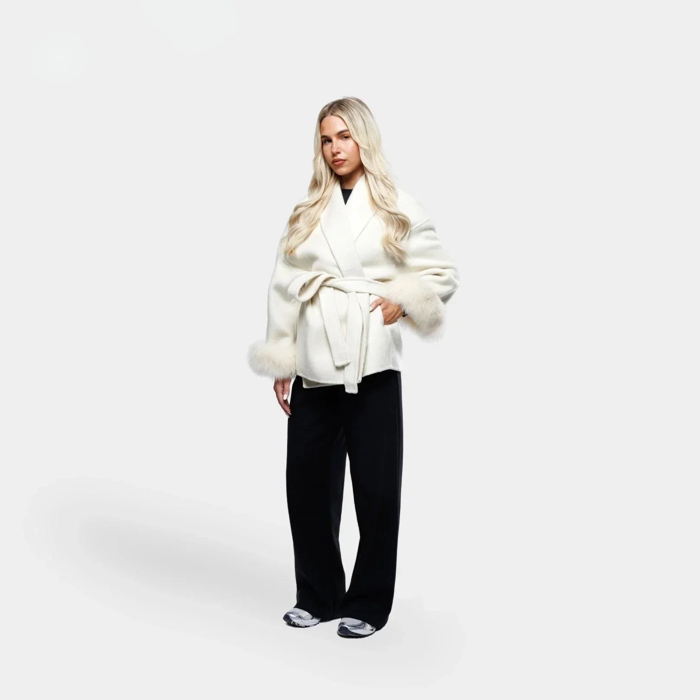 Veste blanche pour femme, ceinturée, avec manches en fourrure synthétique et coupe ajustée.